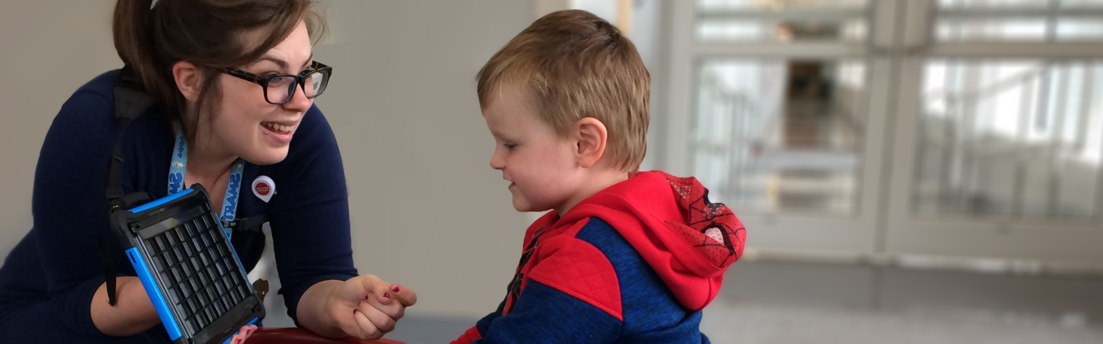 Female clinician communicating with a boy using an augmentative and alternative communication device.