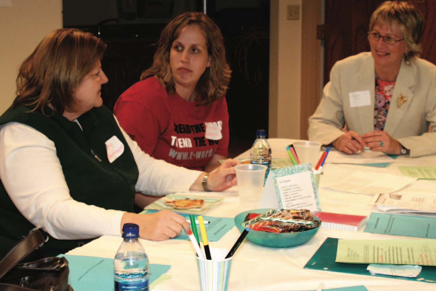 Three women engaged in community conversation at a table