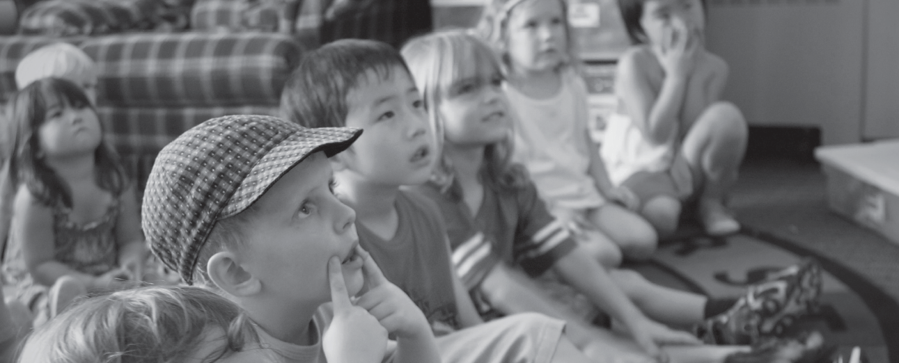 Seven preschoolers sitting on the floor looking up