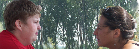 One individual with short hair looking at a woman speaking to her directly across from them. Trees in the background.