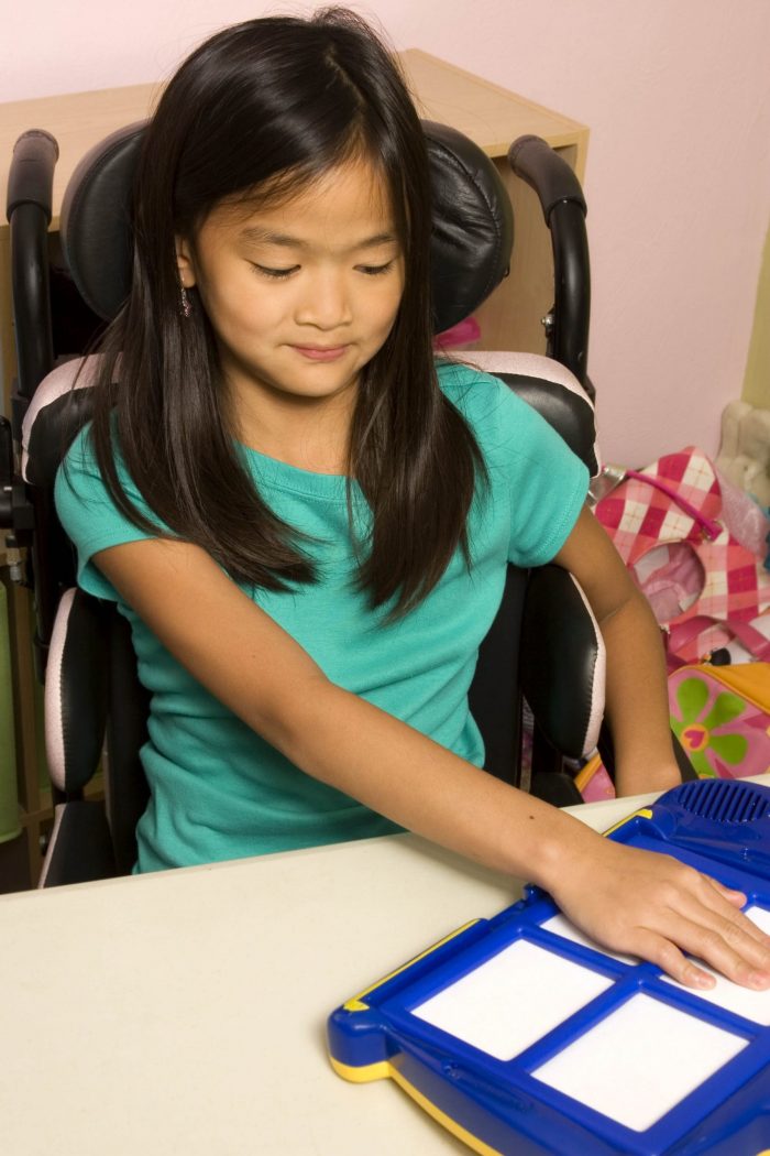 Girl in wheelchair pushes on assistive technology equipment to communicate