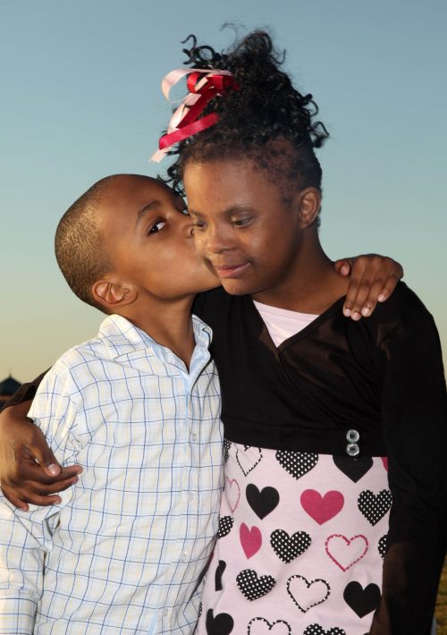 Younger brother giving sister a hug and kiss on cheek